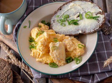 Scrambled eggs with buttered sourdough bread and a cup of coffee on wooden background. 