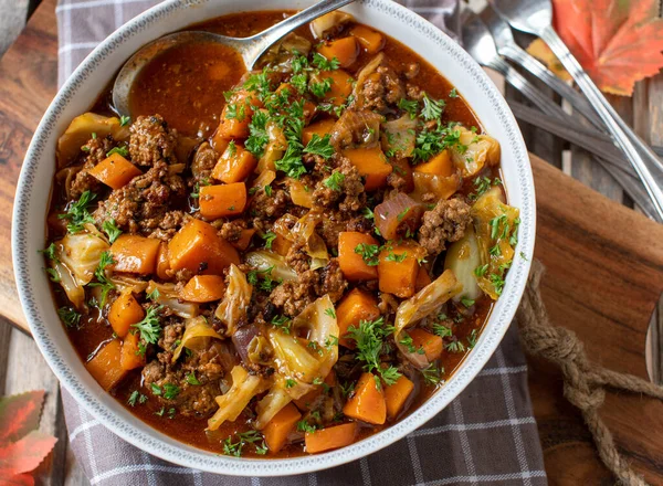Delicious minced meat stew for autumn and winter season cooked with ground beef, cabbage, carrots, onions and herbs. Served in a rustic bowl on wooden background