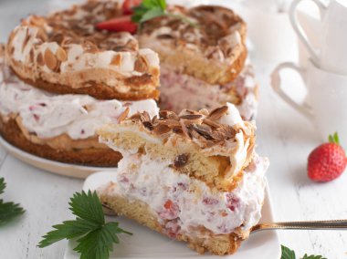 Kremalı çilekli pasta, beyaz masa arkasında badem soslu..