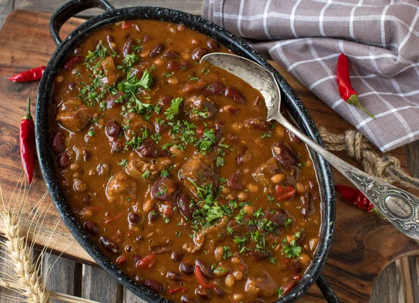 Chili con carne with meat cubes fresh and homemade cooked, Served in a rustic pot on wooden table. Top view