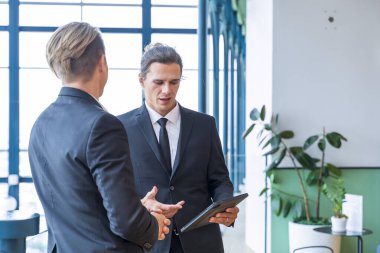 Resmi takım elbiseli Kafkas işadamı, dijital tablet kullanarak modern binada çalışırken tartışıyor.