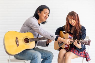 Genç Asyalı genç, müzik sınıfı için basit akorlar gösteren profesyonel bir öğretmenden gitar çalmayı öğreniyor.