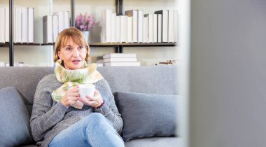 Üst düzey Kafkasyalı kadın rahat bir şekilde kanepede oturup kış boyunca evinde sıcak bez ve eşarpla film izliyor.