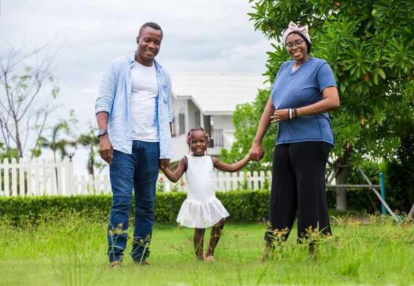 近所の家の外で夏の庭を楽しみながら 緑の草原を歩く若い娘を持つアフリカ系アメリカ人の家族 — ストック写真