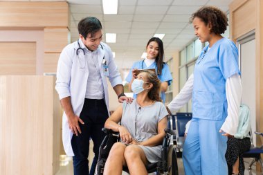 Farklı çeşitlilikteki doktorlardan oluşan bir ekip diz ameliyatından sonra fizik tedavi için hastanedeki tekerlekli sandalyeli kıdemli hastayı keyifle teşvik ediyor.