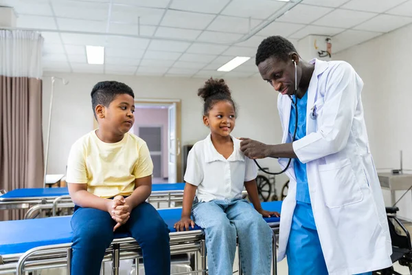 African doctor using stethoscope to diagnose sickness of the young girl while her brother is waiting for his turn nearby in the hospital