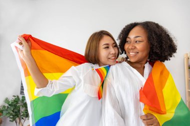 Eşcinsel ve ayrımcılık eşitliği ve farklılıklarını desteklemek amacıyla gurur ayı için LGBTQ gökkuşağı bayrağı taşıyan farklı ırklardan bir çift aynı cinsiyet evliliği