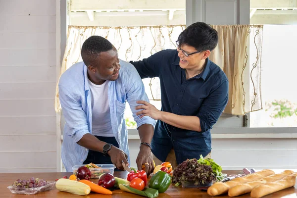 Diversity gender of LGBTQ gay couple between Asian and African ethnicity cooking together at home using organic vegetable to make salad and sandwich