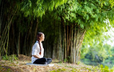 Kadın, sağlıklı akıl ve ruh için iç huzur bilgeliğinden mutluluk elde etmek amacıyla bambu ormanında rahatça meditasyon yapıyor.