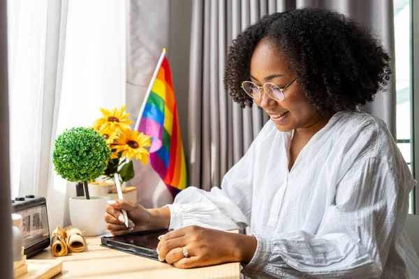 Afro-Amerikalı kız, eşcinsel yönelimde cinsel çeşitlilik ve eşitliği teşvik etmek amacıyla eşcinsel olduğunu açıkladığı için masasında LGBTQ gökkuşağı bayrağı ile çalışıyor.