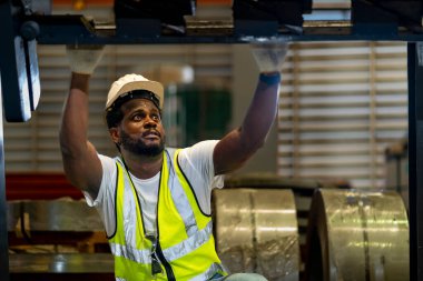 Afrikalı Amerikalı tamirci, bakım ve teftiş için metal çelik fabrikasının içindeki hidrolik makineleri kontrol ediyor.