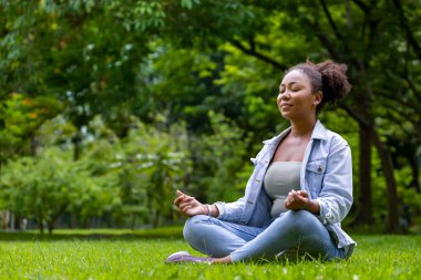 Afrika kökenli Amerikalı kadın, sağlıklı zihin ve ruh kavramları için iç huzur bilgeliğinden mutluluk elde etmek amacıyla ormanda rahatça meditasyon yapıyor.