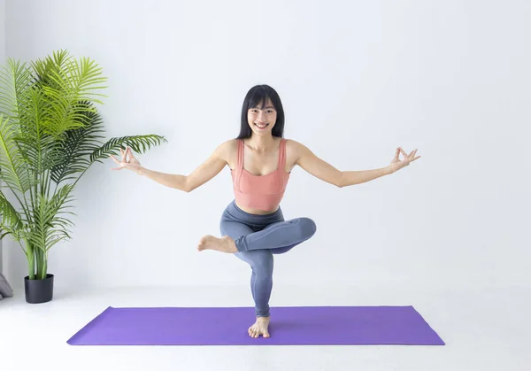 Asian woman practicing yoga indoor with advance balancing position to control breathing in single leg standing position