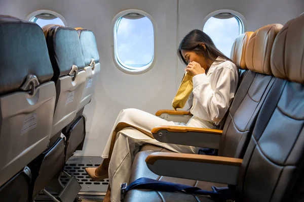 Asian woman is vomitting in the airplane during the flight using vomit bag due to the motion and travel sickness that cause dizzy for aerophobia and air transportation