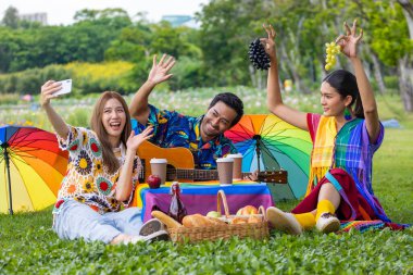 Group of young diversity LGBTQ  friend having a picnic in the garden while enjoy singing music in the outdoor public park during summer with joyful and happiness concept