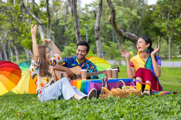 Group of young diversity LGBTQ  friend having a picnic in the garden while enjoy singing music in the outdoor public park during summer with joyful and happiness concept