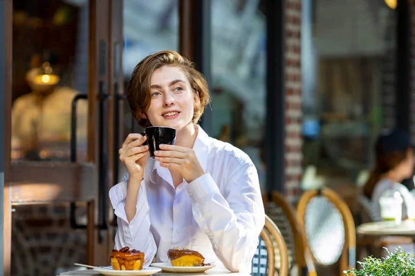 Caucasian woman sipping a hot espresso coffee while sitting outside the european style cafe bistro enjoying slow life with morning vibe at the city square with the sweet pastry