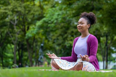 African American woman relaxingly practicing meditation in the forest to attain happiness from inner peace wisdom for healthy mind and soul concept