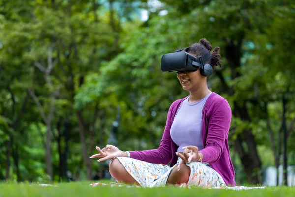 African American woman relaxingly practicing meditation in the forest using VR goggle virtual reality to attain inner peace wisdom for healthy mind and soul in parallel metaverse