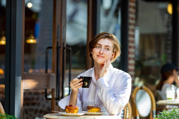 Caucasian woman is sipping a hot espresso coffee while sitting outside the european style cafe bistro enjoying slow life with morning vibe at the city square with sweet pastry