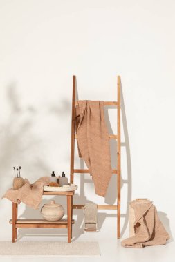 Doğal waffle keten havluları ahşap bankta toprak tonları ve bambu diş fırçaları, rattan sepetleri ve sabun makinesiyle havlu merdiveni. Günlük vücut bakımı, spa ve sıhhat sıfır atık tuvalet kavramı 