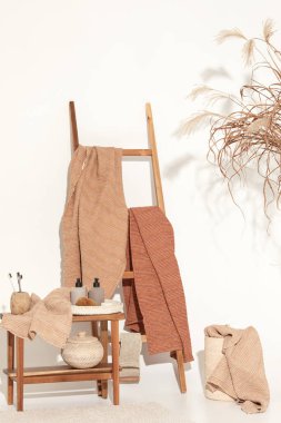 Doğal waffle keten havluları ahşap bankta toprak tonları ve bambu diş fırçaları, rattan sepetleri ve sabun makinesiyle havlu merdiveni. Günlük vücut bakımı, spa ve sıhhat sıfır atık tuvalet kavramı 