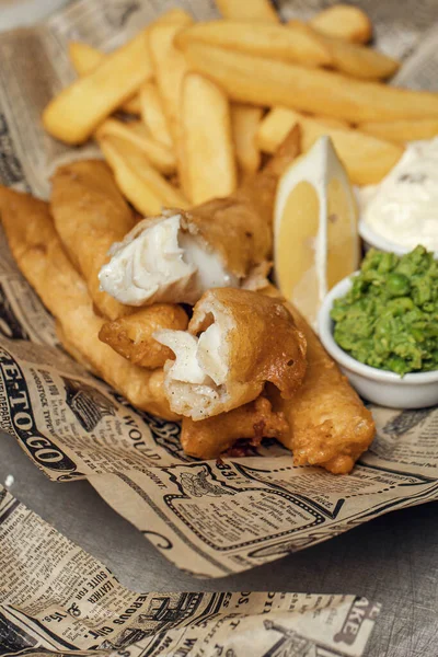 British Traditional crispy Fish and chips with mashed peas, tartar sauce on newspaper