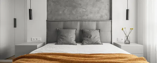 Modern minimalist İskandinav tarzı yatak odası içi turuncu battaniyeyle süslenmiş gri tonlarda. 