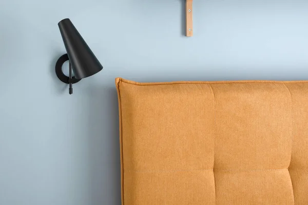 Orange headboard and black minimalistic metal lamp in blue wall. Modern bedroom interior concept