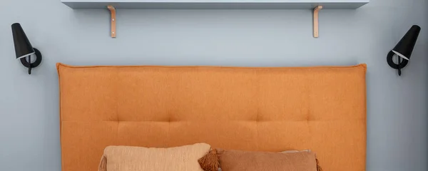 Orange headboard and black minimalistic metal lamp in blue wall. Modern bedroom interior concept