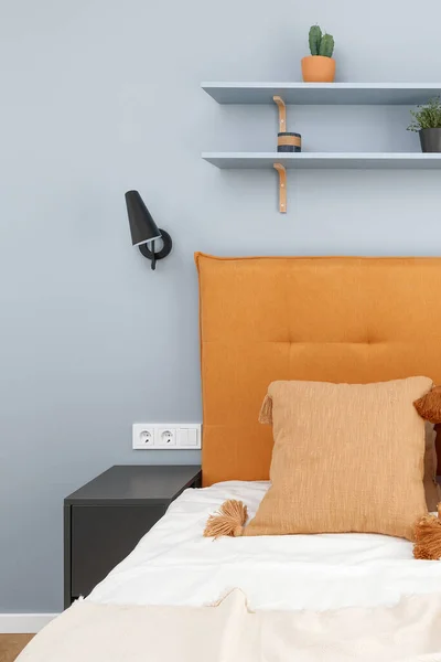 Orange headboard and black minimalistic metal lamp in blue wall. Modern bedroom interior concept