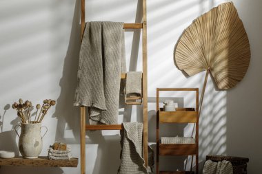 Organik el yapımı sabun, ahşap merdivende asılı keten havlular, bej sabun dağıtıcısı, deri yüzen vücut kayışı ve desenli vazoda kurumuş haşhaş çiçekleri. Sıfır atık banyo aksesuarı