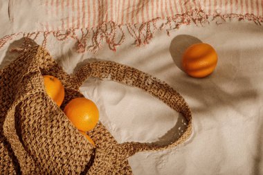 Kumsalda dokuma çantasından taze portakallar dökülüyor. Kenarları olan keten plaj havlusu. Tropik tatil konsepti