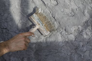 Çatlaklarla ve kusurlarla dolu gri desenli kil duvar oluşturma süreci, fırça kullanarak. Çağdaş iç mekanlarda duvar tasarımı fikirleri. 