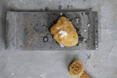 Gri beton tepside köpüklü organik deniz süngeri ve yüz fırçası. Çağdaş banyo içlerindeki banyo aksesuarları. Günlük vücut bakımı, spa ve sıhhat sıfır atık tuvalet kavramı 