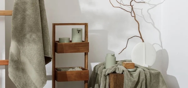 Modern aesthetic bathroom accessories in eucalyptus light  green shade. Organic cotton bath towels, minimalistic Scandinavian style vase, sensor soap and lotion dispenser  on solid oak stump. Daily body care, spa and wellness  bathroom concept