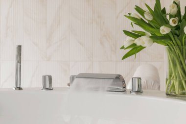 Su lüks ve modern bir musluktan büyük ve modern bir küvete akar. Spa, rahatlama, hijyen konsepti