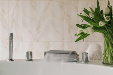 Su lüks ve modern bir musluktan büyük ve modern bir küvete akar. Spa, rahatlama, hijyen konsepti