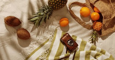 Taze portakallar, ananas, kumsalda örülmüş çantadan dökülen hindistan cevizleri. Çarşaf plaj havlusunda eski bir kamera. Tropik tatil konsepti