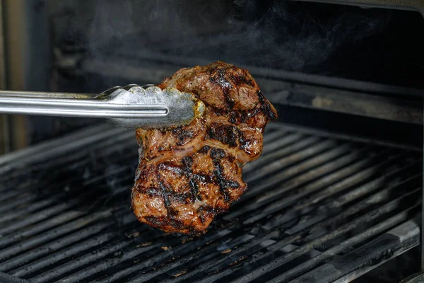 Gümüş servis edilen mutfak maşaları et bifteği ızgara kömür ocağında ızgara ve siyah arka planda duman..