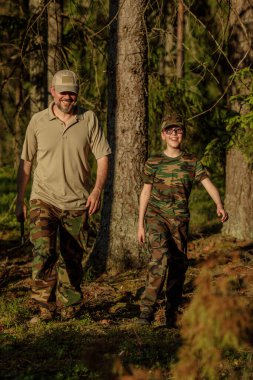 Baba ve oğul askeri kıyafetler içinde ormanda birlikte vakit geçiriyorlar. Macera, seyahat, turizm ve kamp kavramı