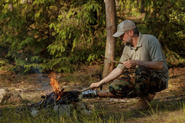 Man in military clothes is making campfire in the woods. The concept of adventure, travel, tourism, camping, survival and evacuation.