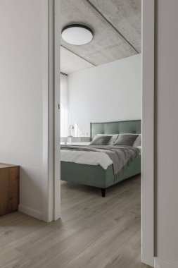 Modern minimalist yatak odası iç tasarımı açık yeşil yataklı gri gölgeler, cam vazoda okaliptüs, beton tavan. İskandinav tarzı. Estetik basit iç tasarım konsepti.