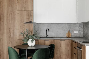 Modern minimalist mutfak ve yemek odası içi ahşap ve beyaz yüzeyler, yeşil sandalyeler ve seramik vazoda okaliptüs. Estetik basit iç tasarım konsepti.
