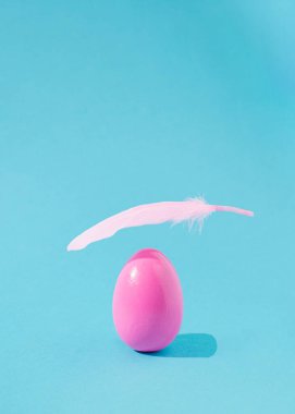 Üstünde yumuşak tüy uçuşan paskalya pembe yumurtası. Açık mavi arkaplan. Bahar tatili estetik modern tasarım