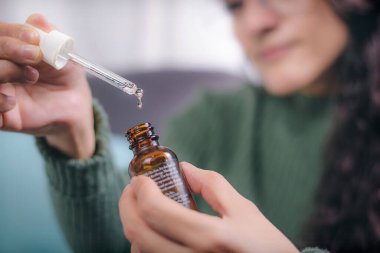 İlgi ve güzellik kavramı. Elinde damlalık olan bir konteynır tutan genç kadının elleri içeriği gösteriyor. Kadın evinde bir koltukta oturuyor..