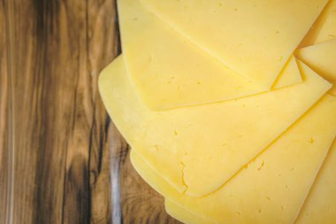 On the table are slices of yellow cheese, approaching a cheese plate.