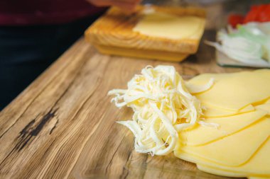 Close-up of a young woman's hands crumbling cheese on a wooden table in a kitchen, preparing a delicious meal.