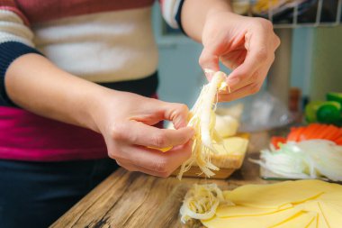 Close-up of a young woman's hands crumbling cheese on a wooden table in a kitchen, preparing a delicious meal.