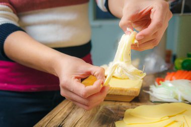Close-up of a young woman's hands crumbling cheese on a wooden table in a kitchen, preparing a delicious meal.